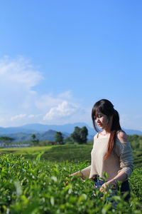 Contemplating woman standing amidst tea plantation field against sky