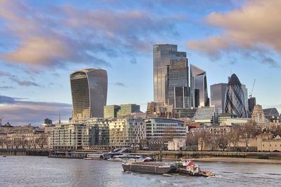 Boats in river by buildings against sky in city