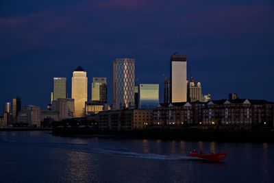 Illuminated buildings by river against sky in city at night