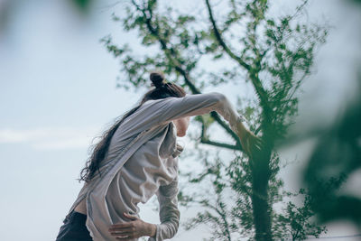 Low angle view of woman by tree against sky