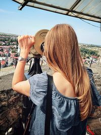 Rear view of woman looking through coin-operated binoculars at cityscape