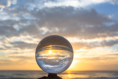 Close-up of crystal ball on beach against sky during sunset