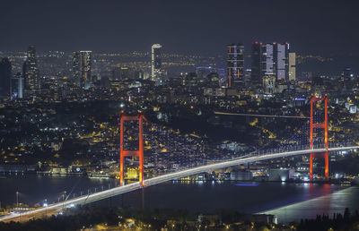 Illuminated bridge over river by buildings against sky at night