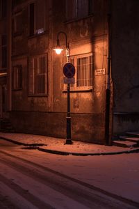 Illuminated street light on sidewalk by building at night