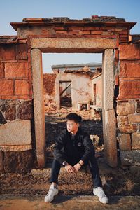 Full length of man sitting on abandoned building