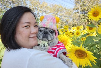 Portrait of woman carrying dog at sunflower farm