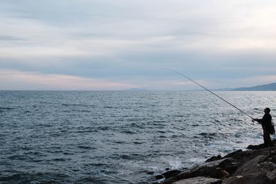 Man fishing in sea against sky