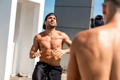 Young shirtless men exercising against sky outdoors
