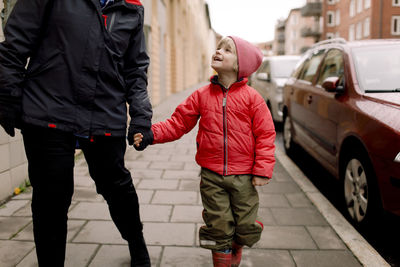 Smiling grandson in warm clothing holding hands of grandmother while walking on footpath