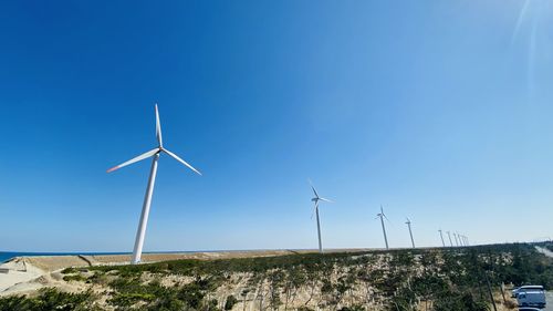 Wind turbines on landscape against clear blue sky