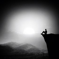 Side view of man sitting on cliff edge against sky