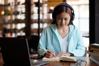 Young woman writing in book at library