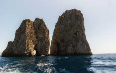 Rock formation in sea against clear sky