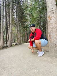 Full length of smiling man crouching in forest