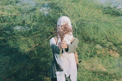 Woman holding bunch of dry flowers while standing on field