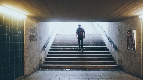 Rear view of man walking on staircase at underground walkway