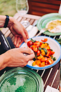 Cropped image of person preparing salad in bowl on table outdoors