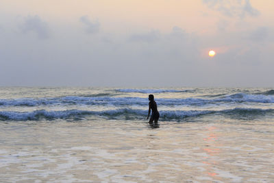 Woman in sea against sky during sunset