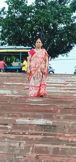 Full length of woman with arms raised against tree