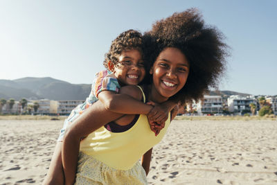 Happy girl piggybacking sister at beach