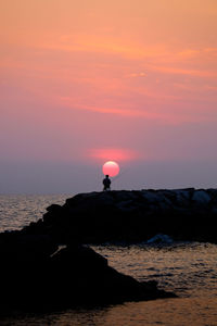 Silhouette man fishing against orange sky during sunset