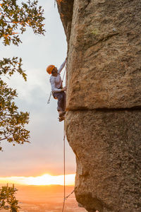 Male mountaineer climbing high cliff with safety carabiner and ropes