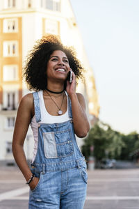 Smiling young woman talking on mobile phone against buildings