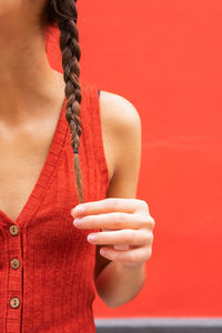 Crop young female touching pigtails on red background in street