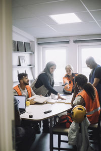 Female carpenter discussing over wooden block with colleagues at desk in warehouse office