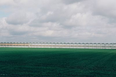 Built structures in front of grassy field against cloudy sky