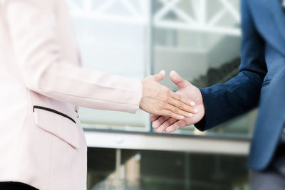 Midsection of business people doing handshake while standing against building