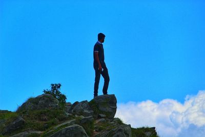 Rear view of man standing on rock against blue sky