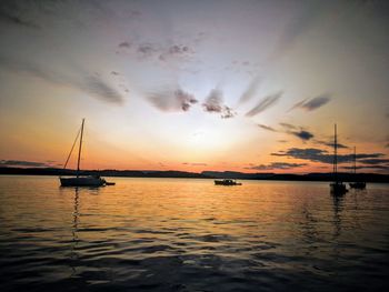 Silhouette boats sailing in sea against dramatic sky during sunset