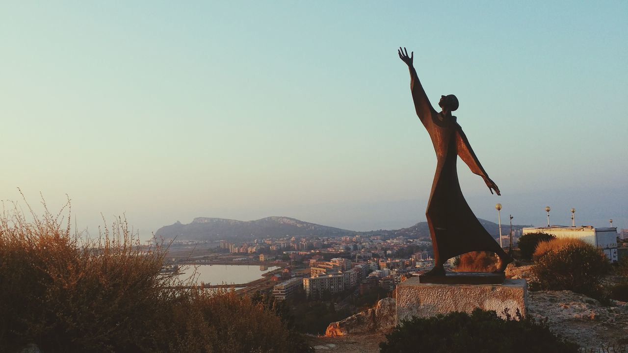 clear sky, statue, sculpture, copy space, water, built structure, architecture, human representation, building exterior, art and craft, cityscape, art, city, creativity, sky, animal representation, travel destinations, outdoors, dusk