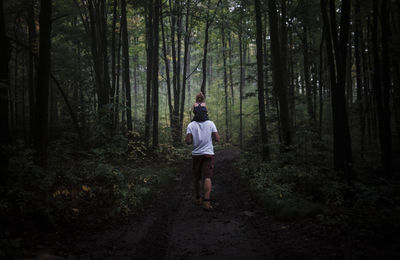 Rear view of father carrying daughter on shoulders at forest