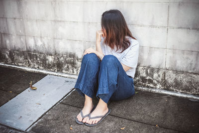 Full length of woman sitting on footpath