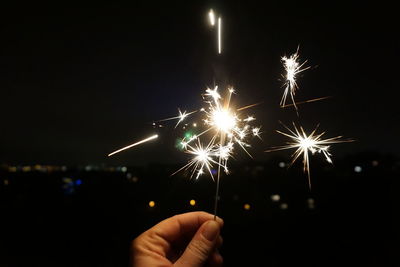 Cropped hand holding sparkler against sky at night