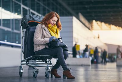 Woman sitting on push cart at airport