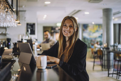 Portrait of smiling female professional sitting with laptop at bar counter in restaurant