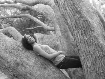 Smiling woman relaxing on tree trunk at forest
