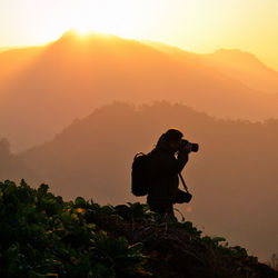 Man photographing on mountain against sky during sunset