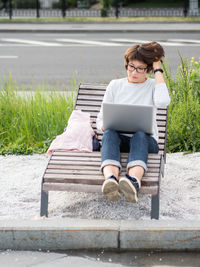 Woman sits with laptop on urban park bench. freelancer at work. student learns remotely