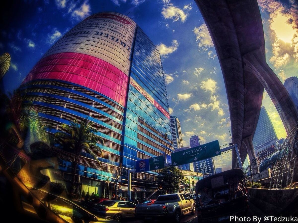 architecture, building exterior, built structure, sky, city, modern, low angle view, skyscraper, cloud - sky, tall - high, car, transportation, land vehicle, office building, tower, cloud, city life, mode of transport, illuminated, building