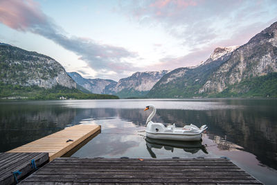 Swan shaped pedal boat in river against sky during sunset