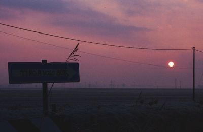 Road sign on field against sky at sunset