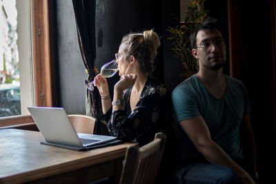 Man sitting by woman drinking wine by laptop on table in bar 