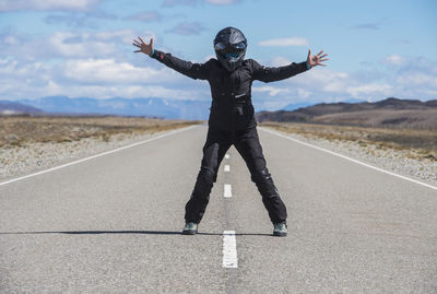 Woman in motorbike gear standing in the middle of empty highway