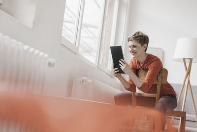 Smiling woman sitting on chair using tablet