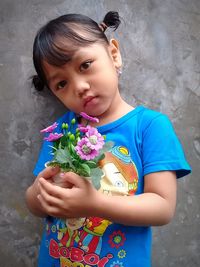 Low angle view of girl holding flower standing against wall