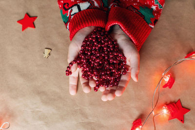 A red christmas garland in children's hands lies on the table